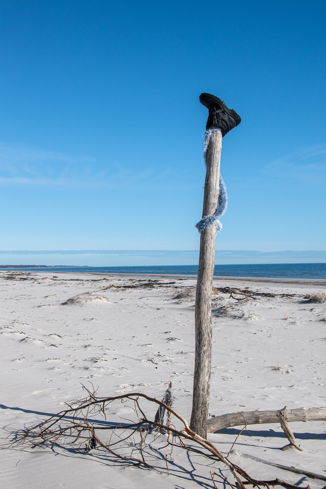 En svart känga upphängd på en stolpe på en strand.